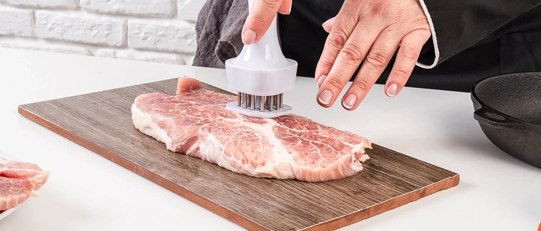 A chef tenderizing a steak on a wooden board