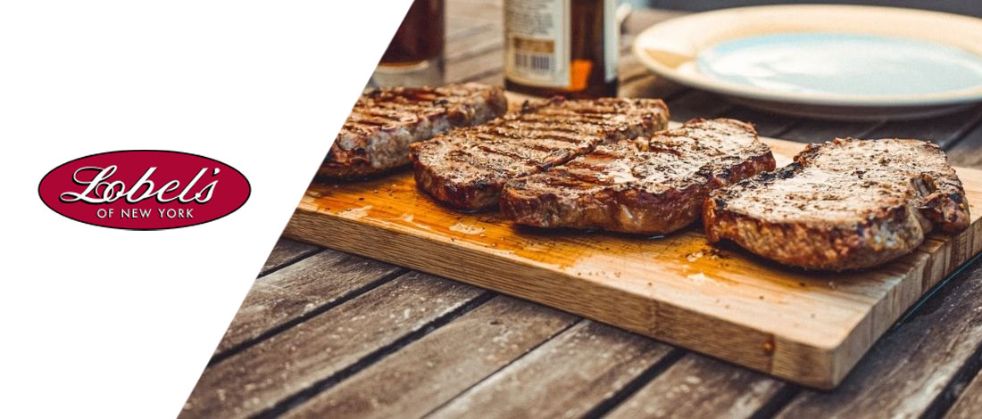 A row of steak on a wooden chopping board beside the Lobel's of New York logo