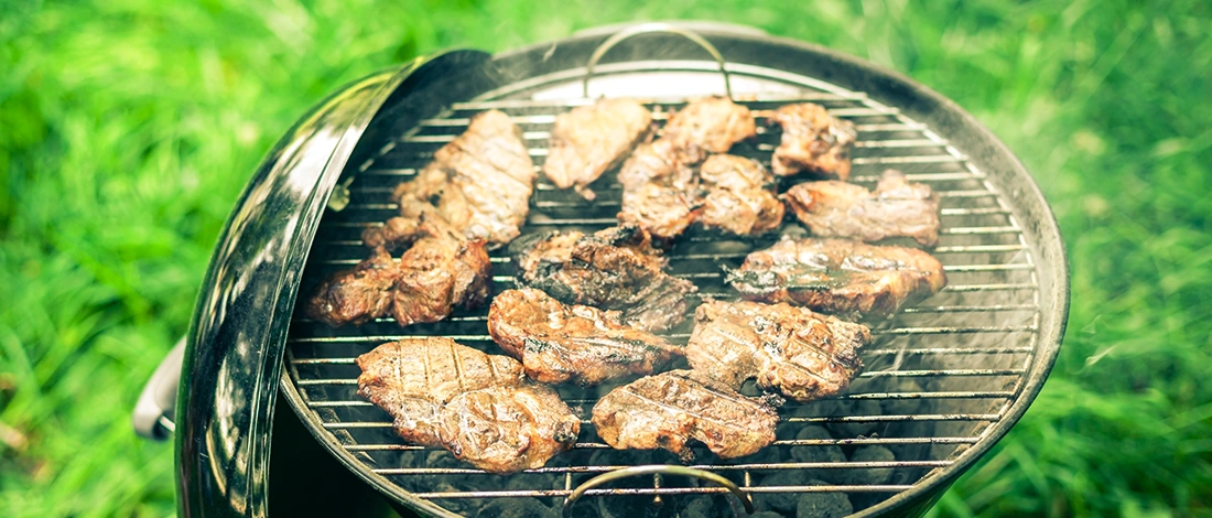 A portable grill outdoors cooking meat patties