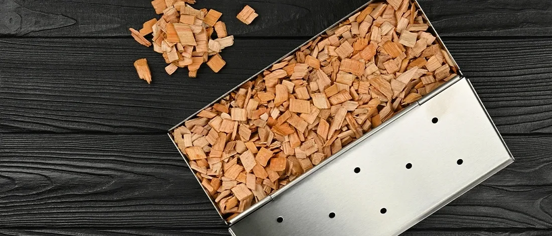 A metal smoker box with wood chips inside