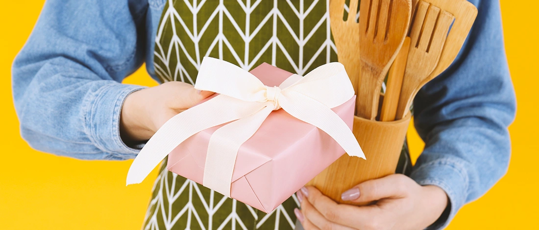 Someone holding a pink giftbox with wooden cooking utensils