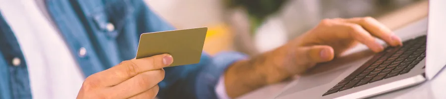 A person using a laptop while holding a credit card