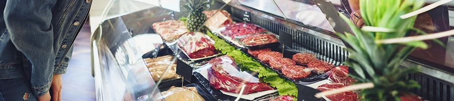 A person beside a glass showcase with different meats