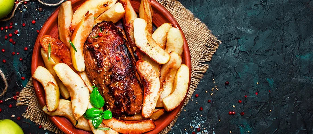 An image of cooked meat with apples on a plate