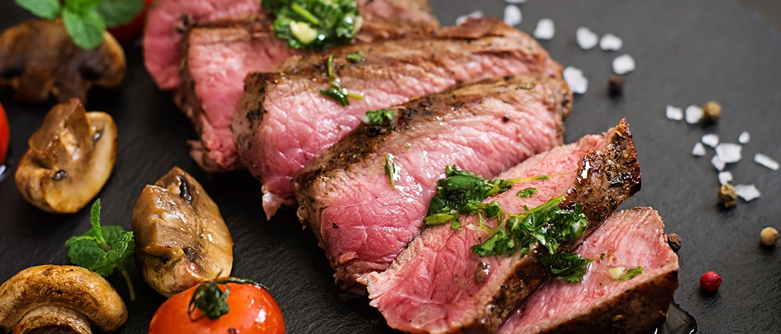 A close up image of medium rare steak with mushrooms and other spices