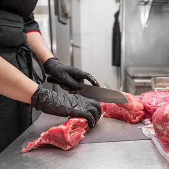A chef wearing black gloves cutting raw meats