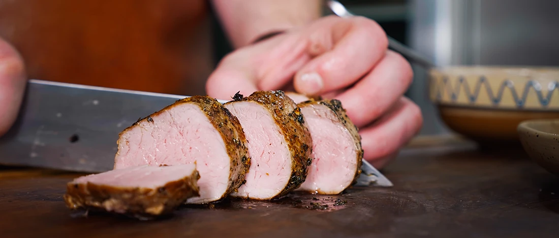 A woman slicing pink pork steak